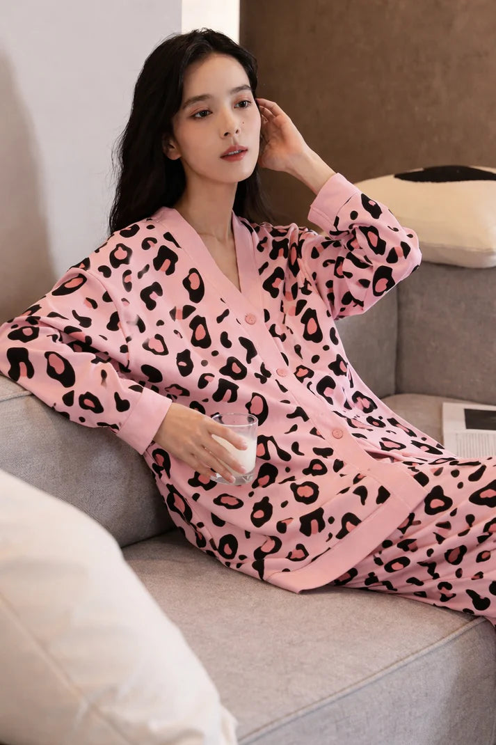 Woman in pink leopard print pajama set sitting on a couch holding a glass of milk.