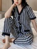 Person wearing a black and white houndstooth pattern pajama set on a bed.