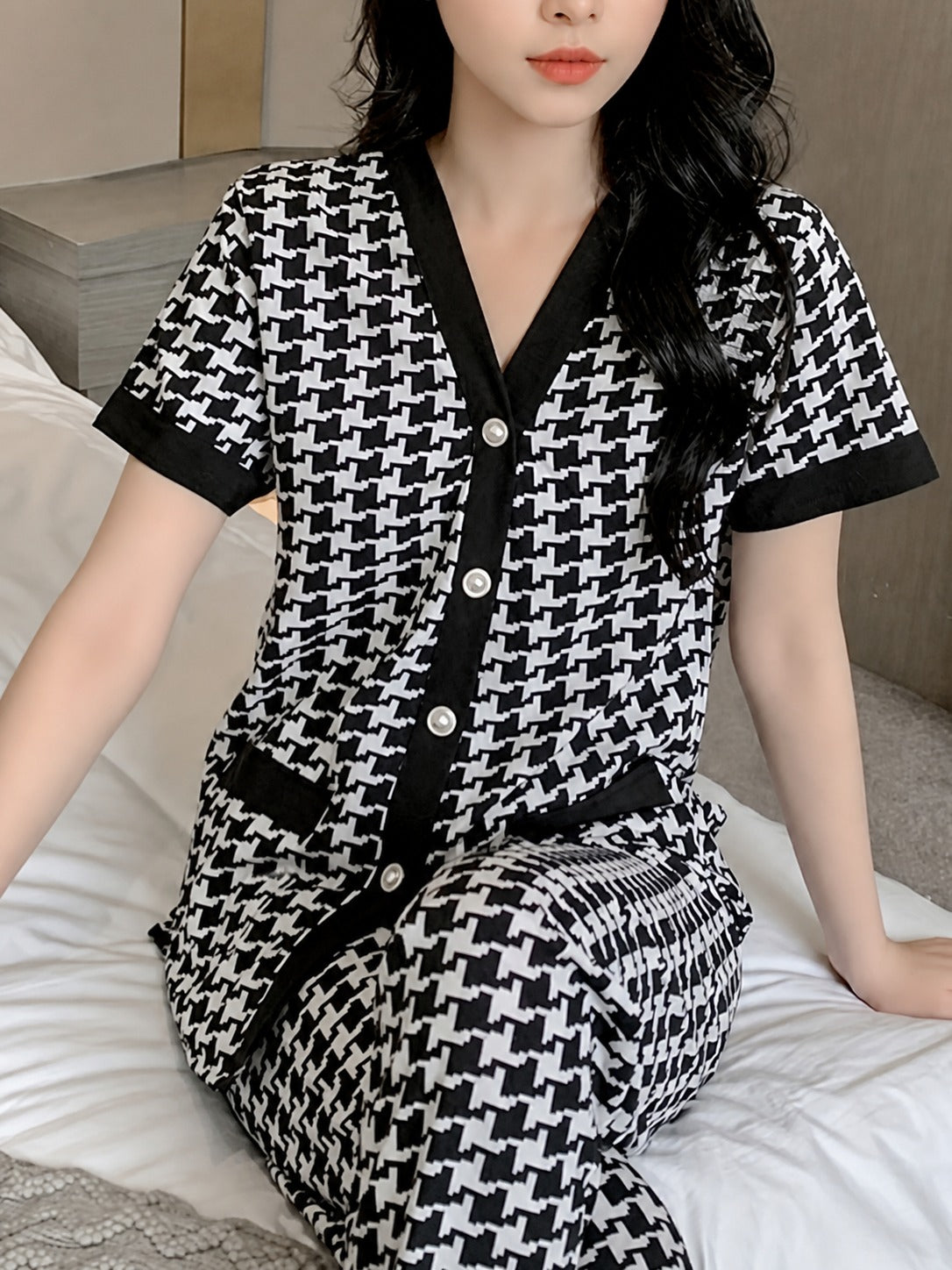 Person wearing a black and white patterned outfit sitting on a bed.